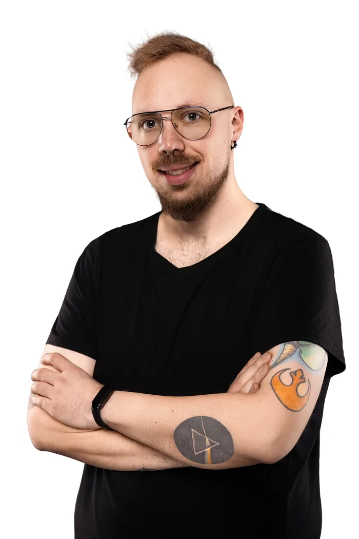 Paweł Nowik uśmiechnięty, w czarnej koszulce, ze skrzyżowanymi rękami, na jasnym tle